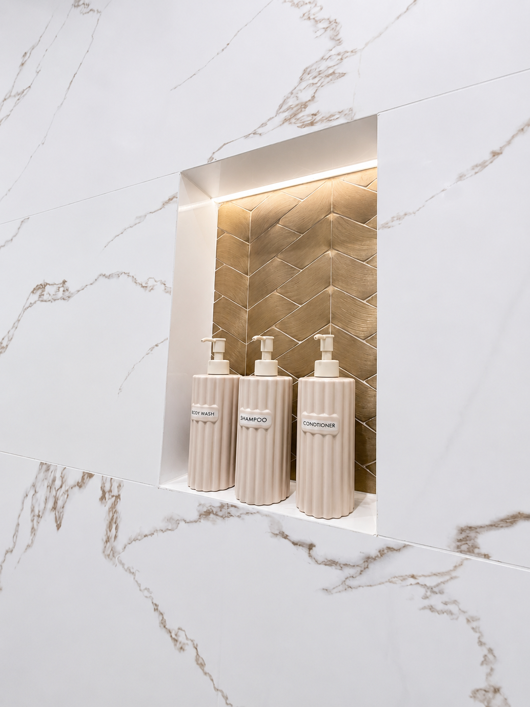 Backlit shower niche in marble bathroom with brushed brass herringbone feature tile