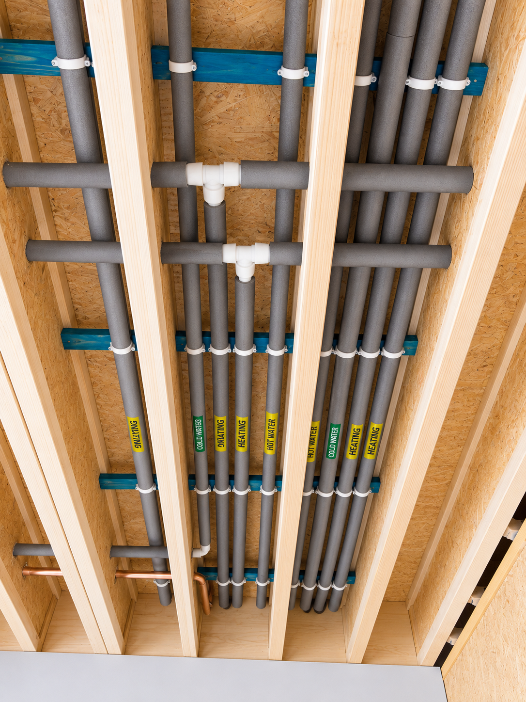 Labelled hot water, cold water and heating pipes neatly clipped to timber joists during first fix